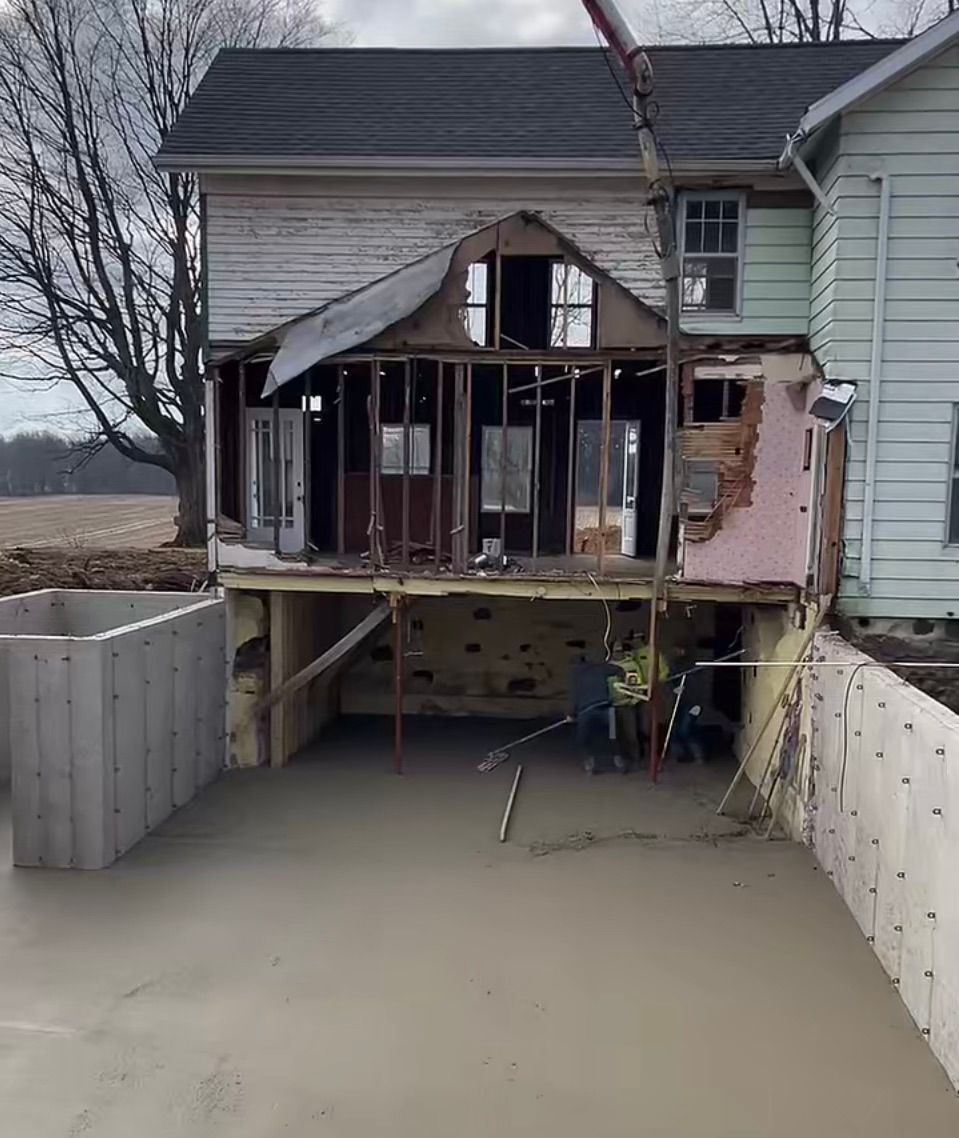 A house is being demolished and a concrete driveway is being poured in front of it.