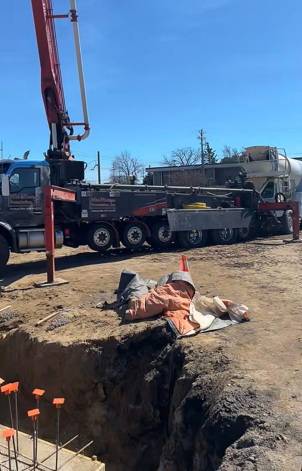 A concrete pump truck is pumping concrete into a hole in the ground.