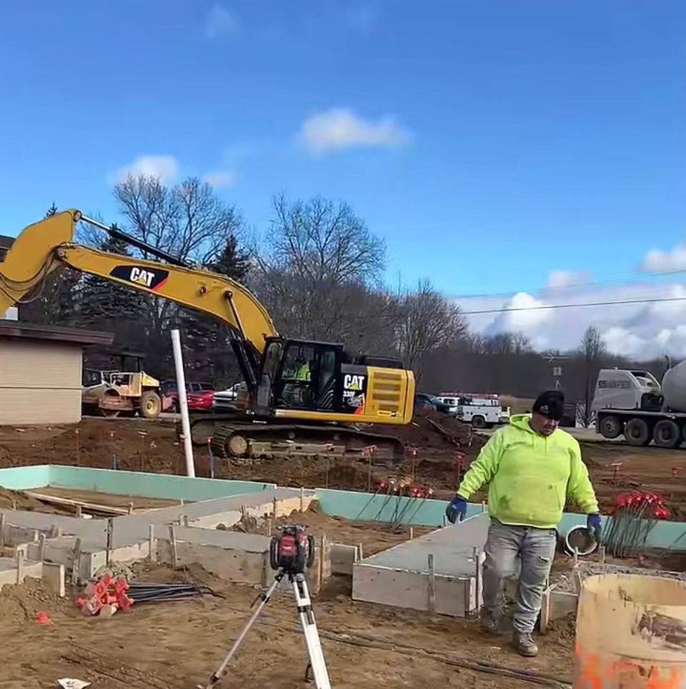 A man in a neon green jacket is standing in front of a construction site.