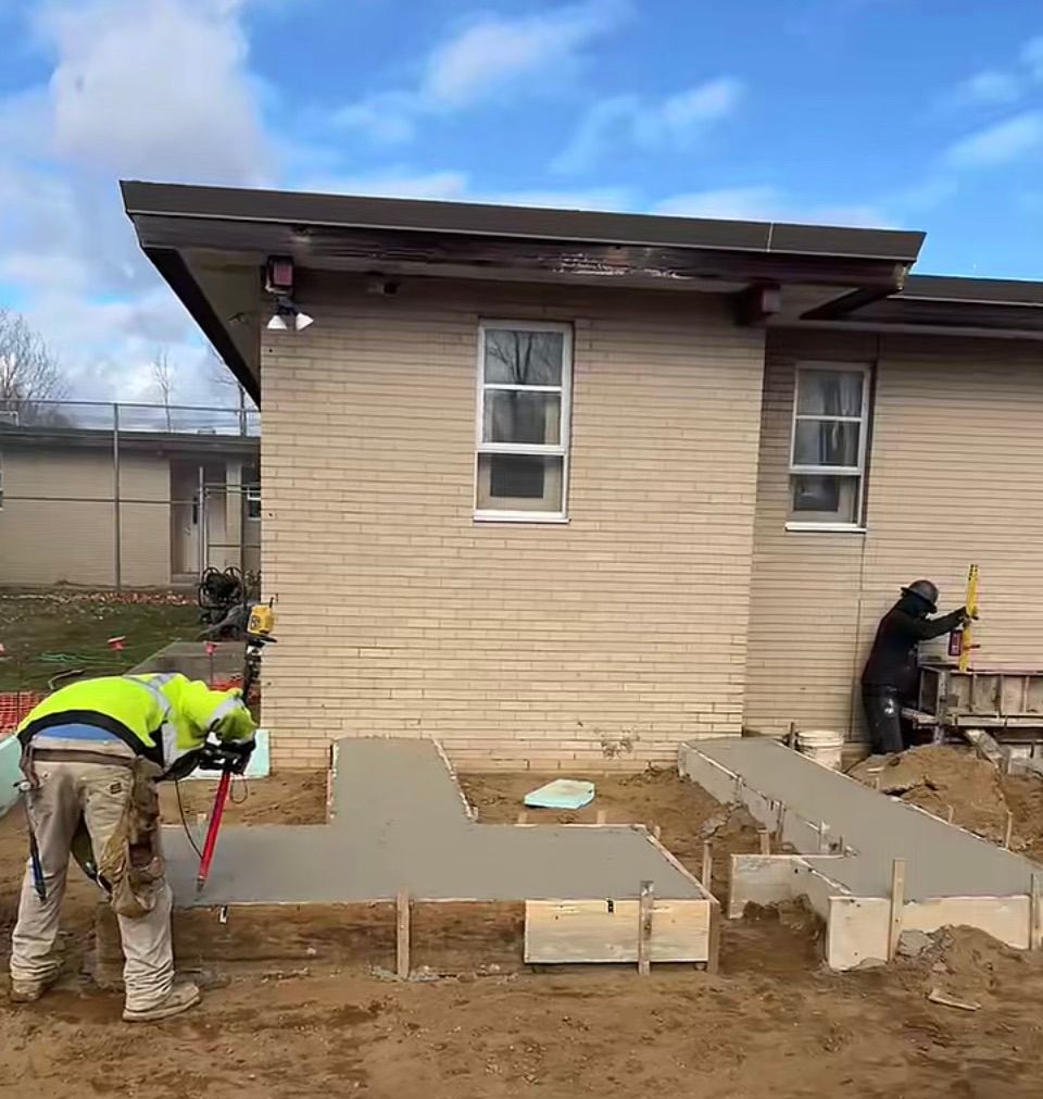 A group of construction workers are working on a concrete walkway in front of a house.