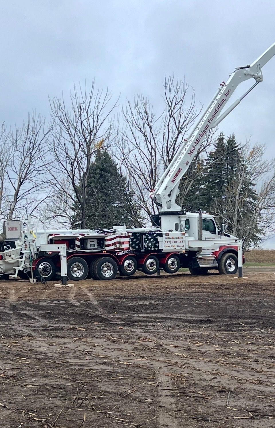 A red and black truck with a crane attached to it is parked in a dirt field.