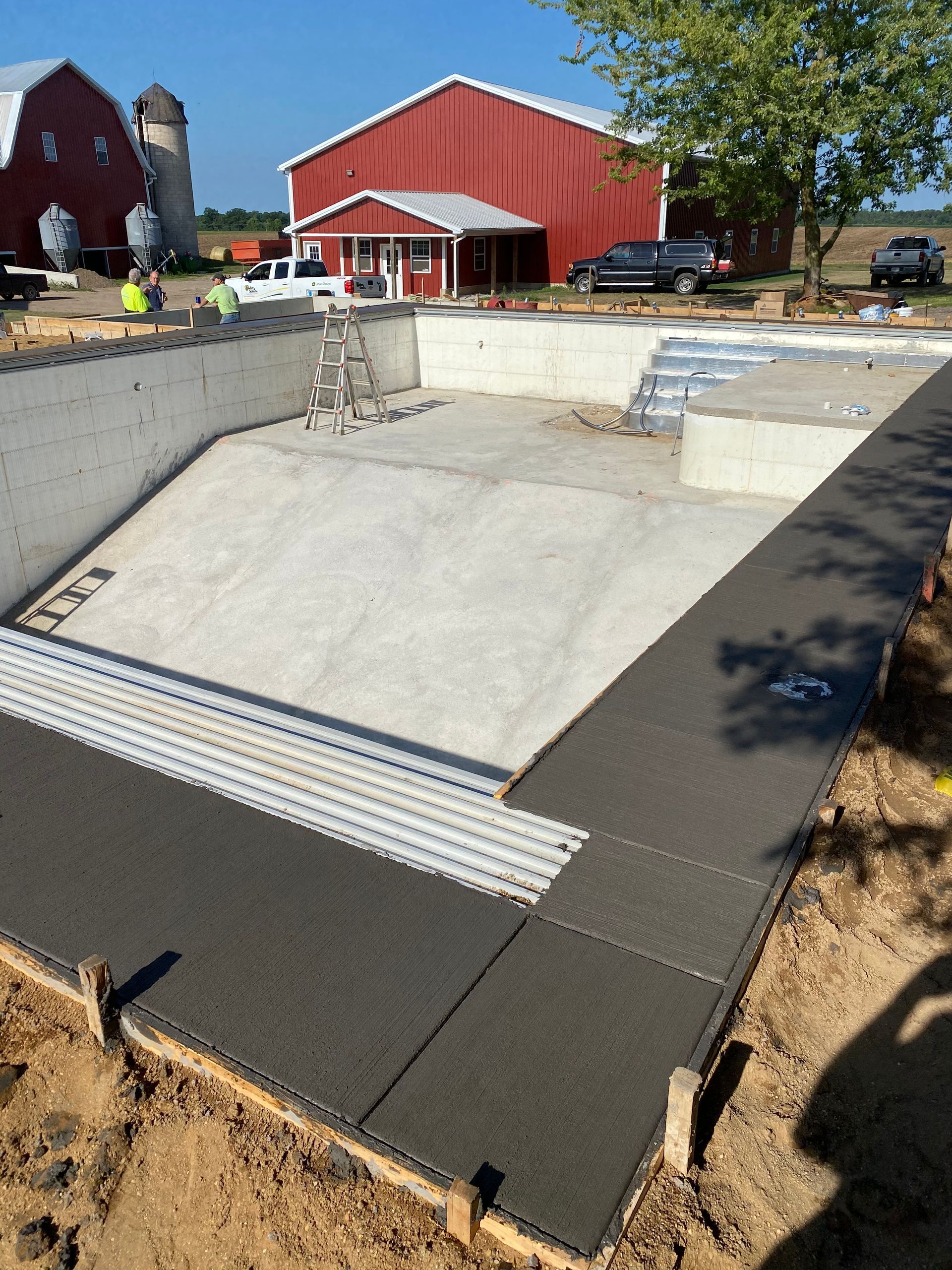 A swimming pool is being built in front of a red barn.
