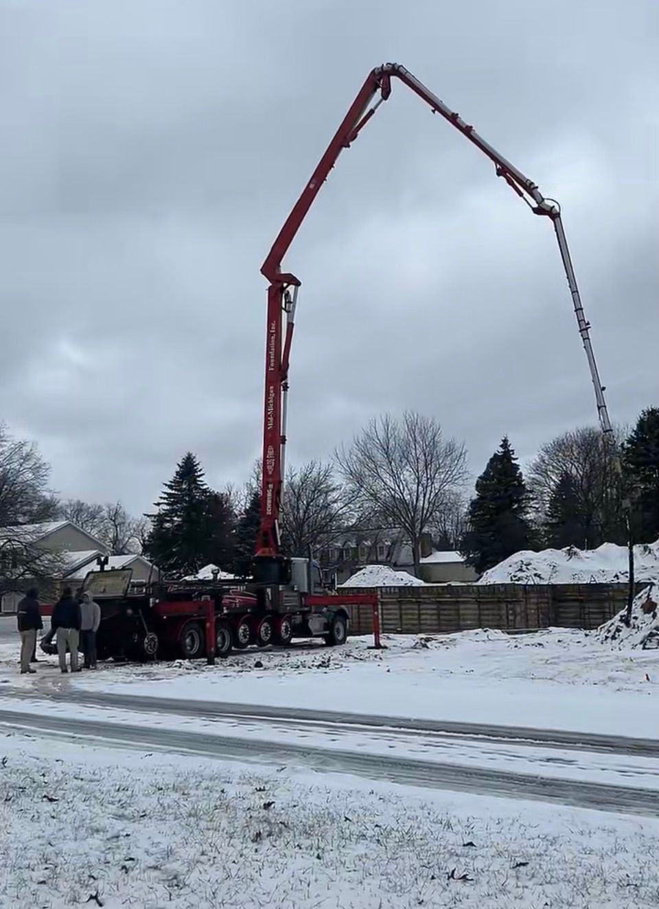 A concrete pump is being used to pour concrete on a snowy road.