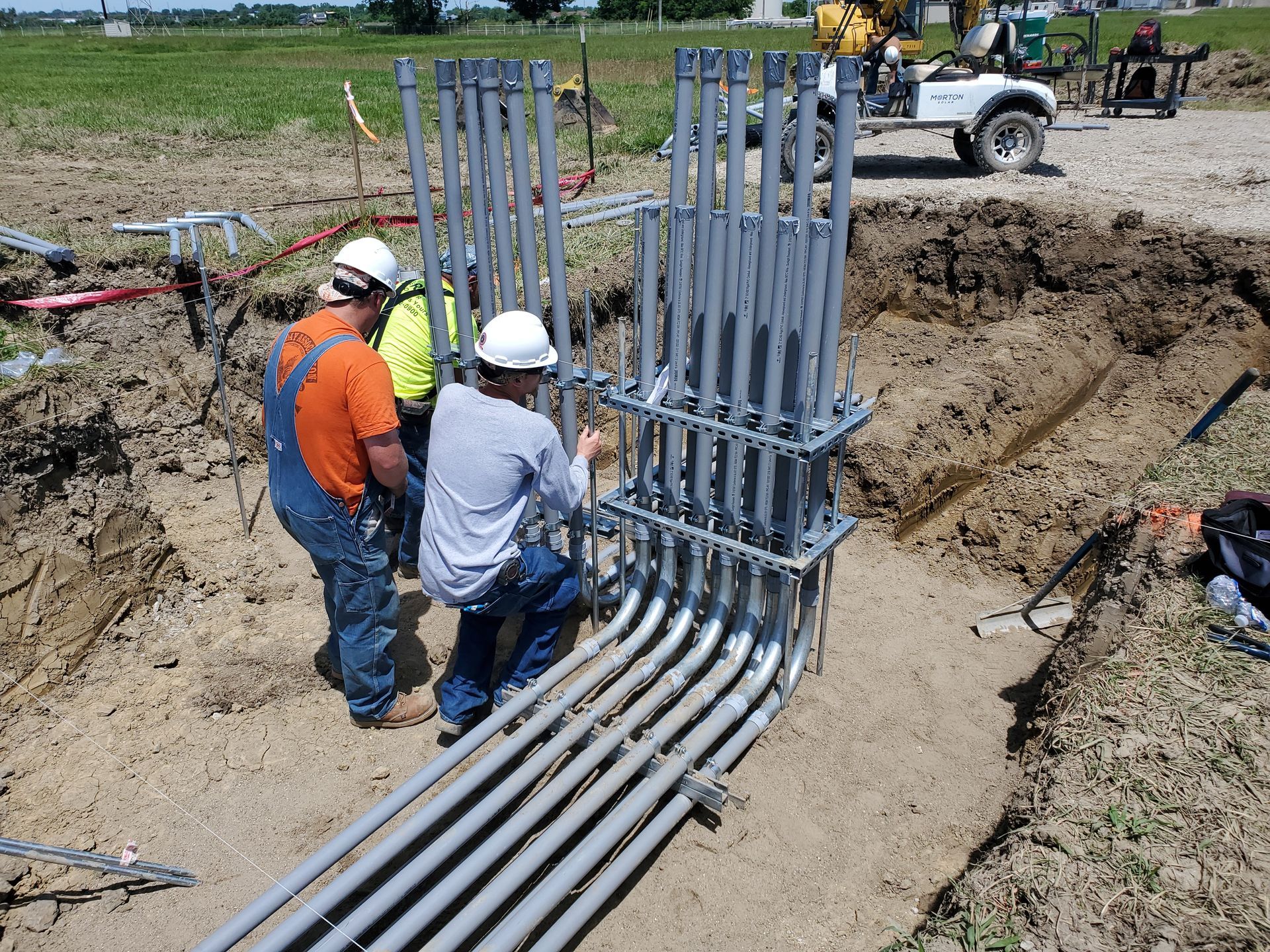 Two workers are working on metal piping for wiring a power panel.