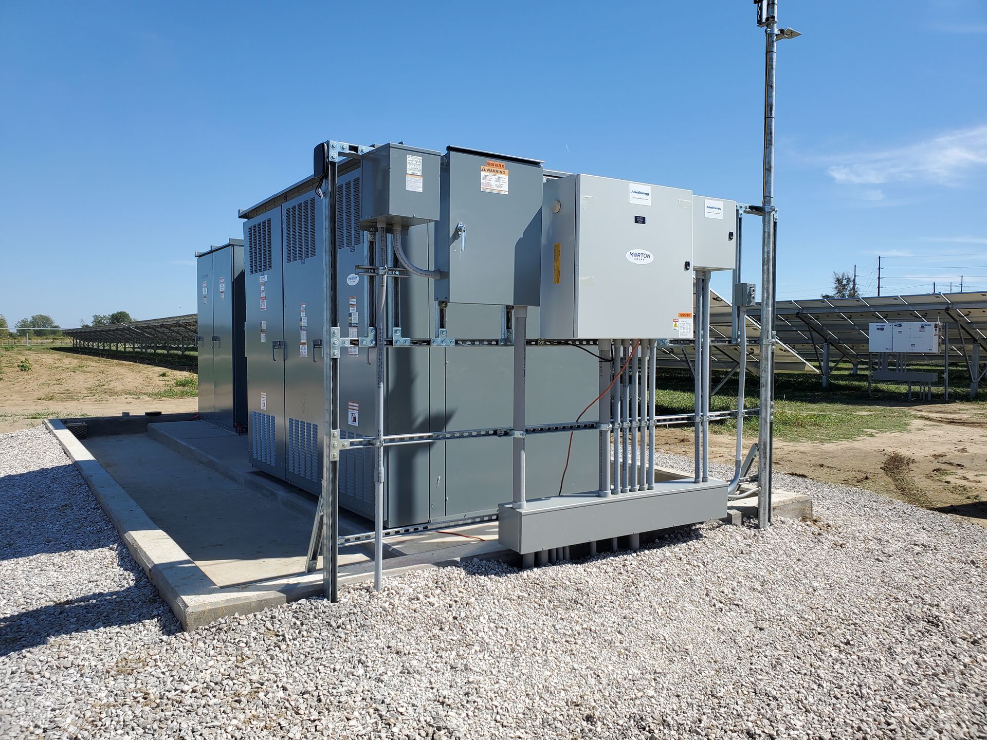 A large electrical box is sitting in the middle of a gravel field.