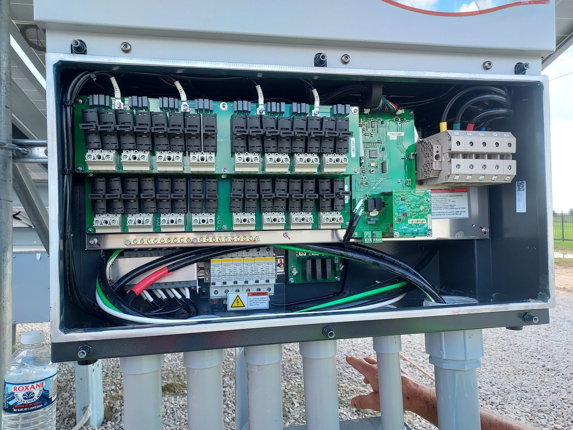 Solar panel junction box with circuit boards, wires, and connectors, mounted outdoors.