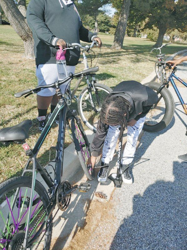 JCB Academy Bike Club - Principal fixing bike tire outdoors, two others stand nearby.
