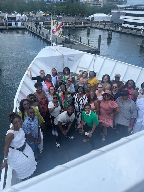 Group of people smiling on a boat deck; water, pier, and Maryland flag visible.