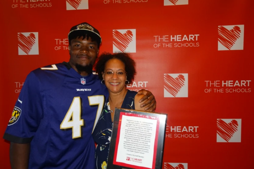 HOS Honors - Ravens Player with woman holding an award, posing in front of a red backdrop with 