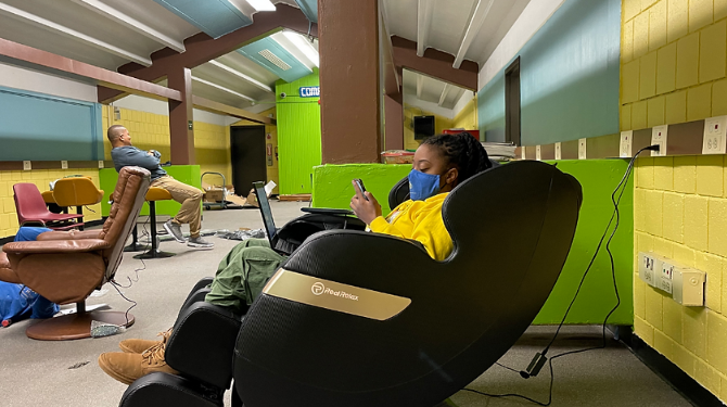Student working on their phone and laptop in a chair
