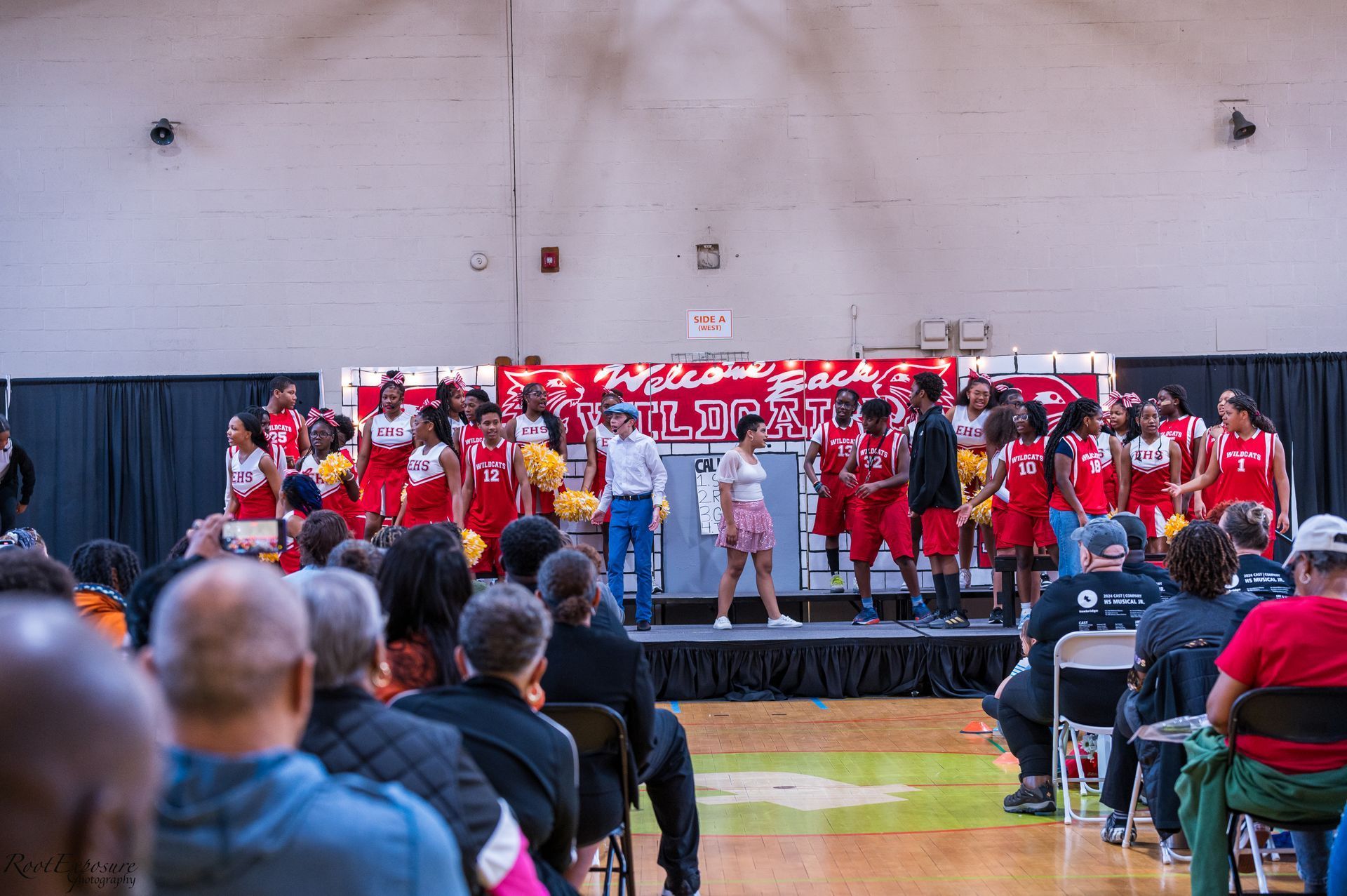 Turnbridge School Pep Rally - People watch a performance on a stage inside a gymnasium. The performers wear red and white uniforms.