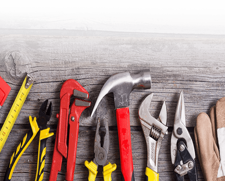 Herramientas alineadas sobre madera desgastada: cinta métrica, alicates, llave inglesa, martillo, tijeras y guantes.