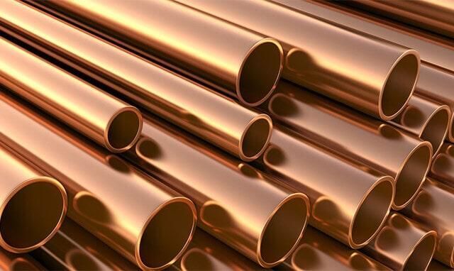 Tubos de cobre apilados entre sí, reflejando la luz con un color marrón anaranjado brillante.