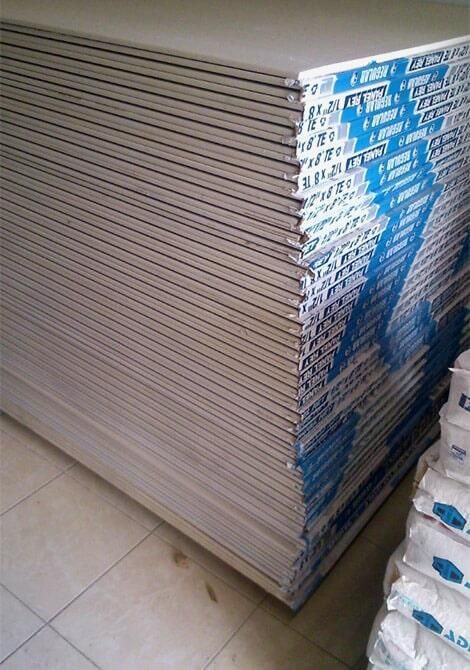 Pila de láminas de yeso con una marca azul en el borde, apoyada sobre un piso de color claro.