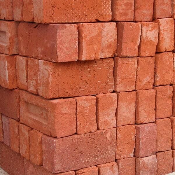 Pila de ladrillos rojos, vista de esquina, que muestra texturas y variaciones de color.