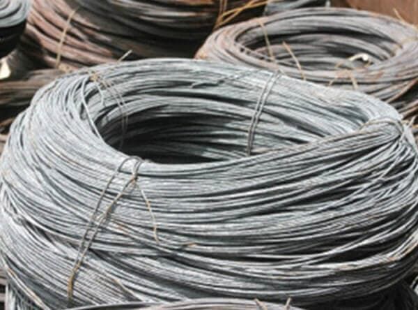 Bobinas de alambre gris, posiblemente de acero, apiladas al aire libre.