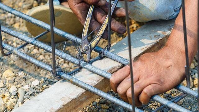 Persona que utiliza alicates para asegurar el alambre en las barras de refuerzo de acero durante la construcción.
