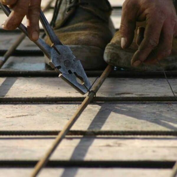 Persona que utiliza alicates para asegurar la rejilla de varillas de refuerzo de metal con una bota en la parte superior.