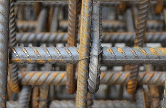 Primer plano de una rejilla de varillas de refuerzo de acero, unida con alambre, que muestra barras texturizadas y óxido.