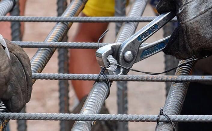 Un trabajador utiliza alicates para torcer alambre y asegurar las barras de refuerzo en un sitio de construcción.