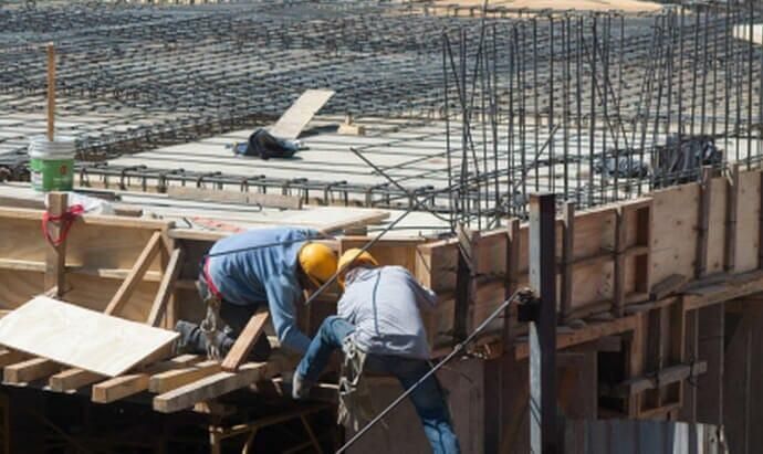 Obreros de la construcción con cascos trabajando con encofrados de madera y barras de refuerzo en una obra en construcción.