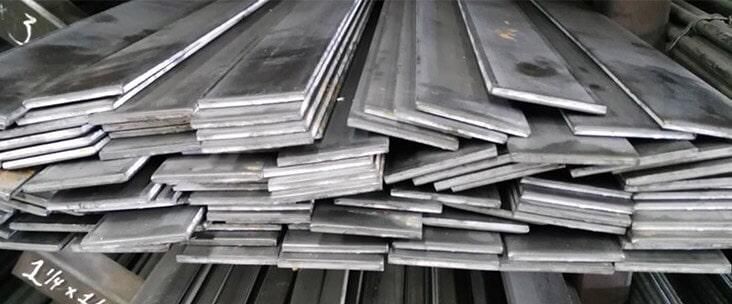 Pila de barras metálicas planas, posiblemente de acero, de distintas longitudes y espesores.