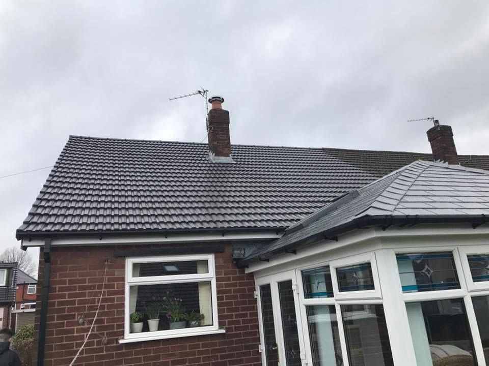 Brick house with a dark tiled roof, a chimney, and a white-framed window. Cloudy sky.