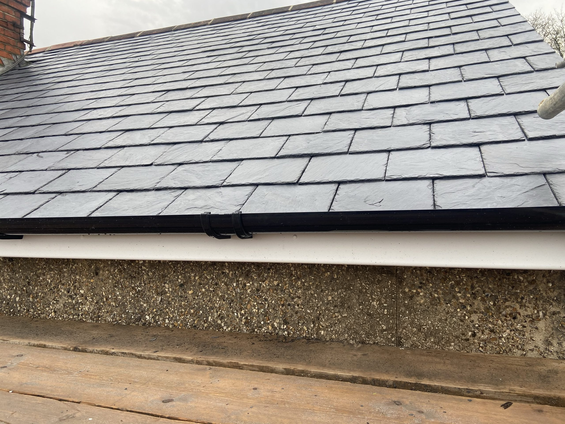 Dark slate roof with black fascia and white gutter over a textured wall.