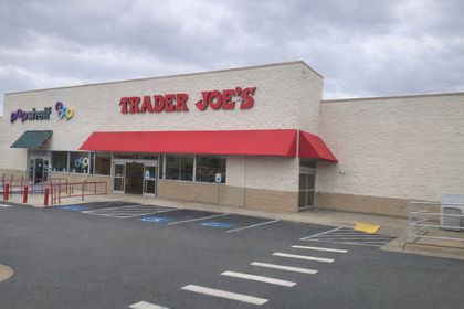 A Trader Joe's storefront with a red awning under a cloudy sky, located in a shopping center with an adjacent parking lot.