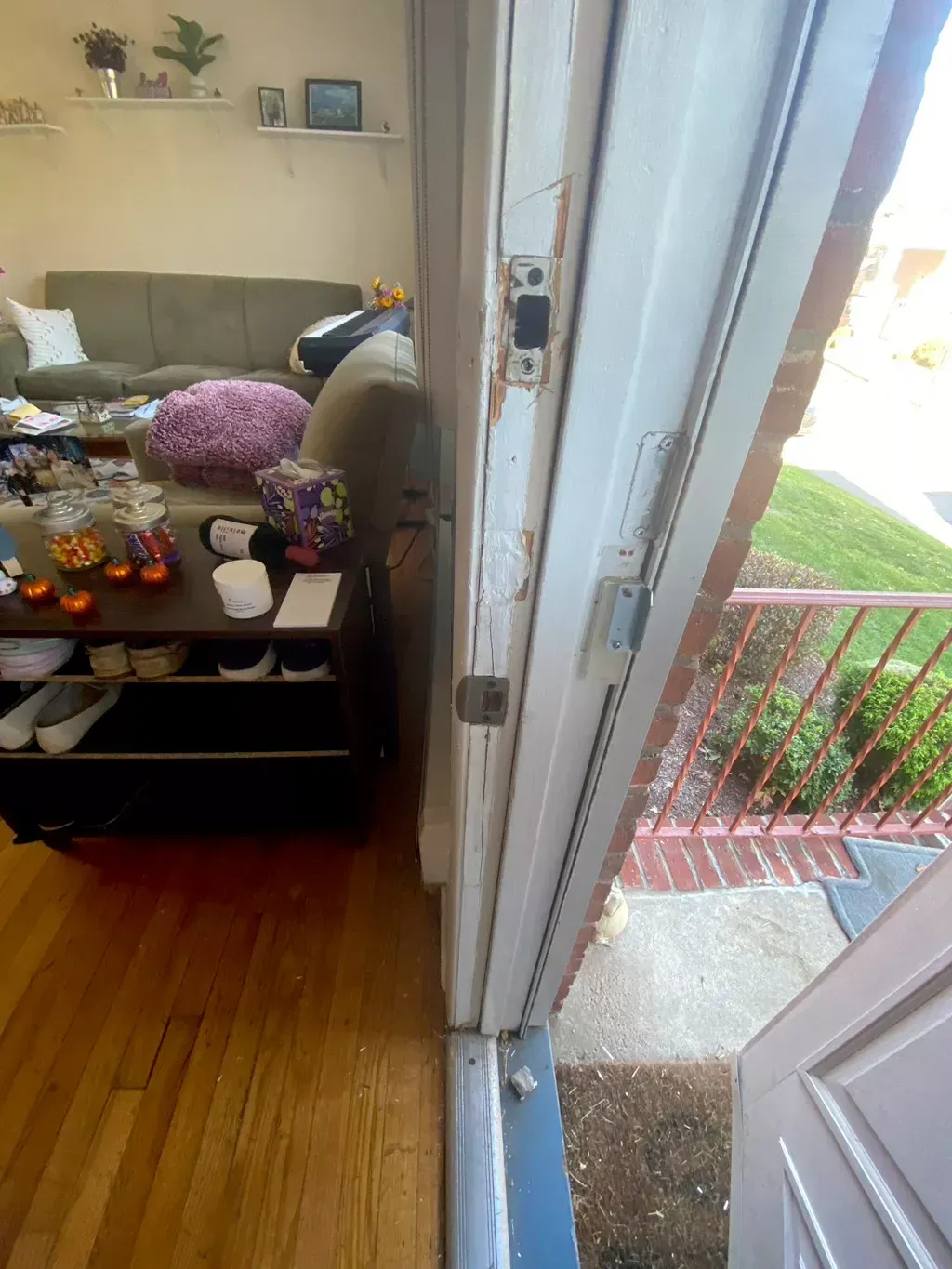 A partially open white door with locks, revealing an interior living room and an exterior brick porch.