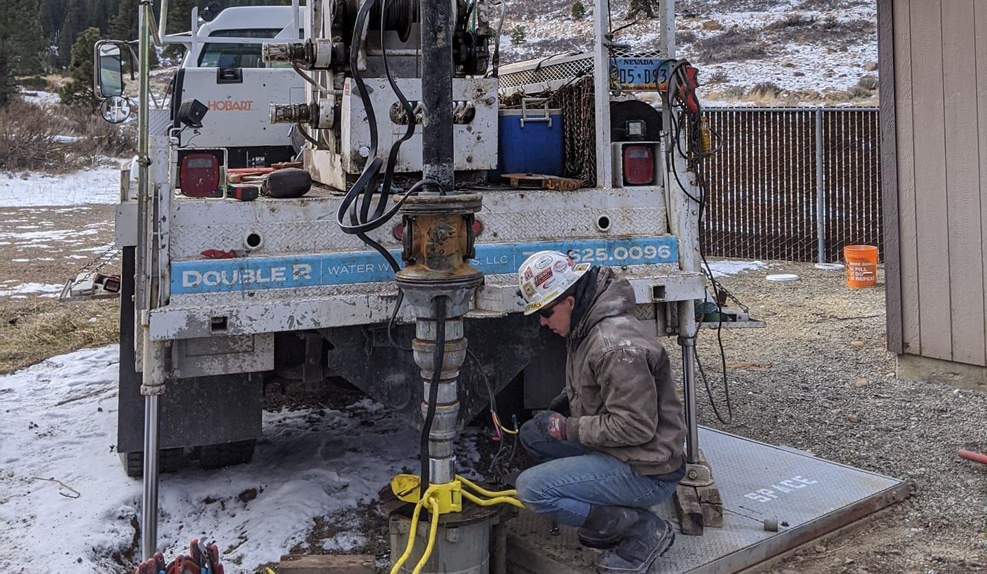 A man wearing a hard hat is working on a machine in front of a truck.