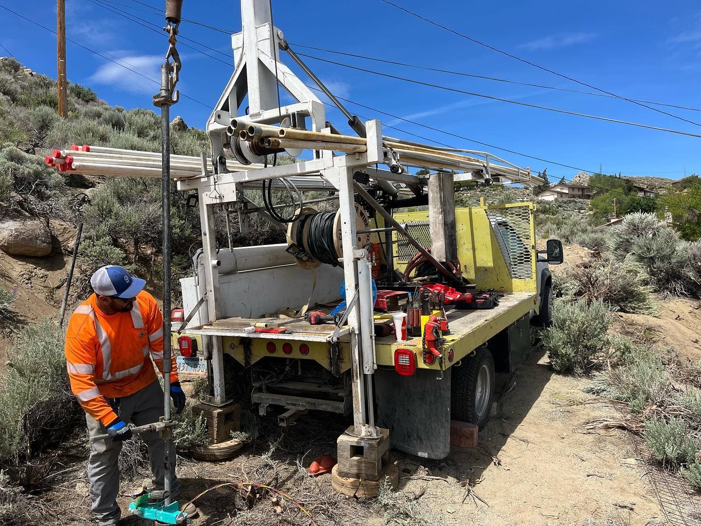 Man in orange vest operates a drilling rig on a truck, outdoors.
