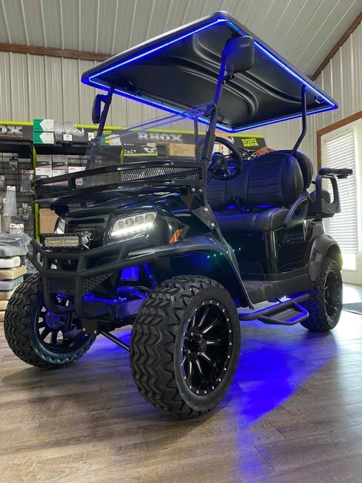 A black golf cart with blue lights on the roof is parked in a garage.