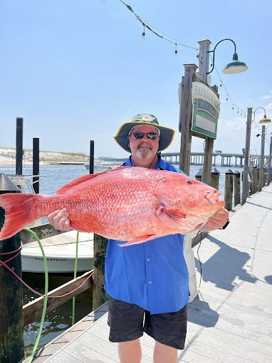 A man is holding a large red fish on a dock.