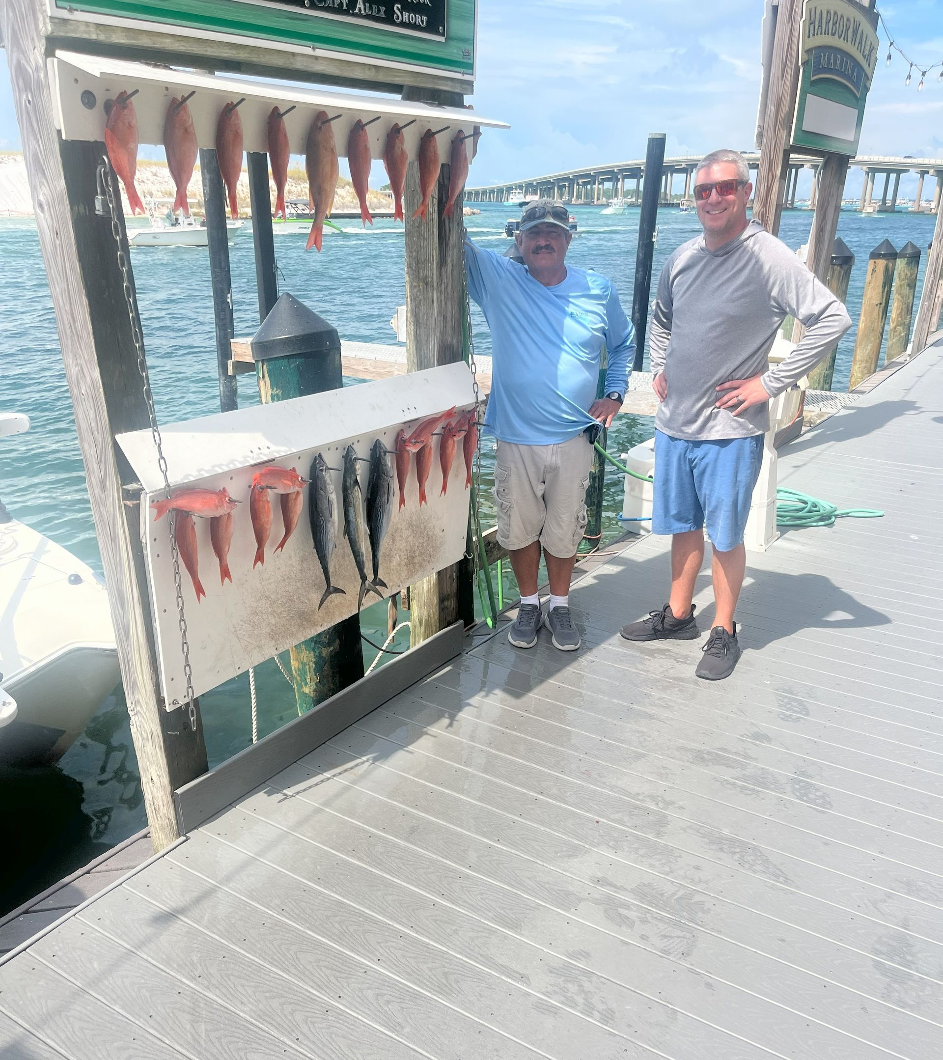 Two men are standing on a dock next to a display of fish.