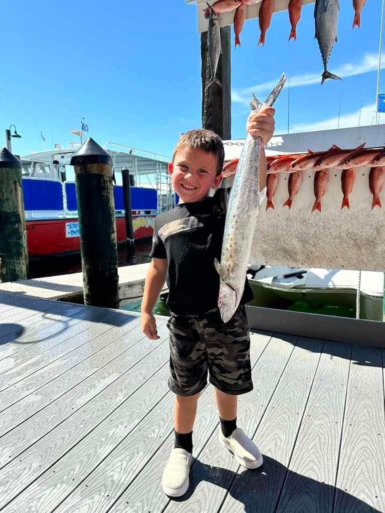 A young boy is holding a large fish on a dock.