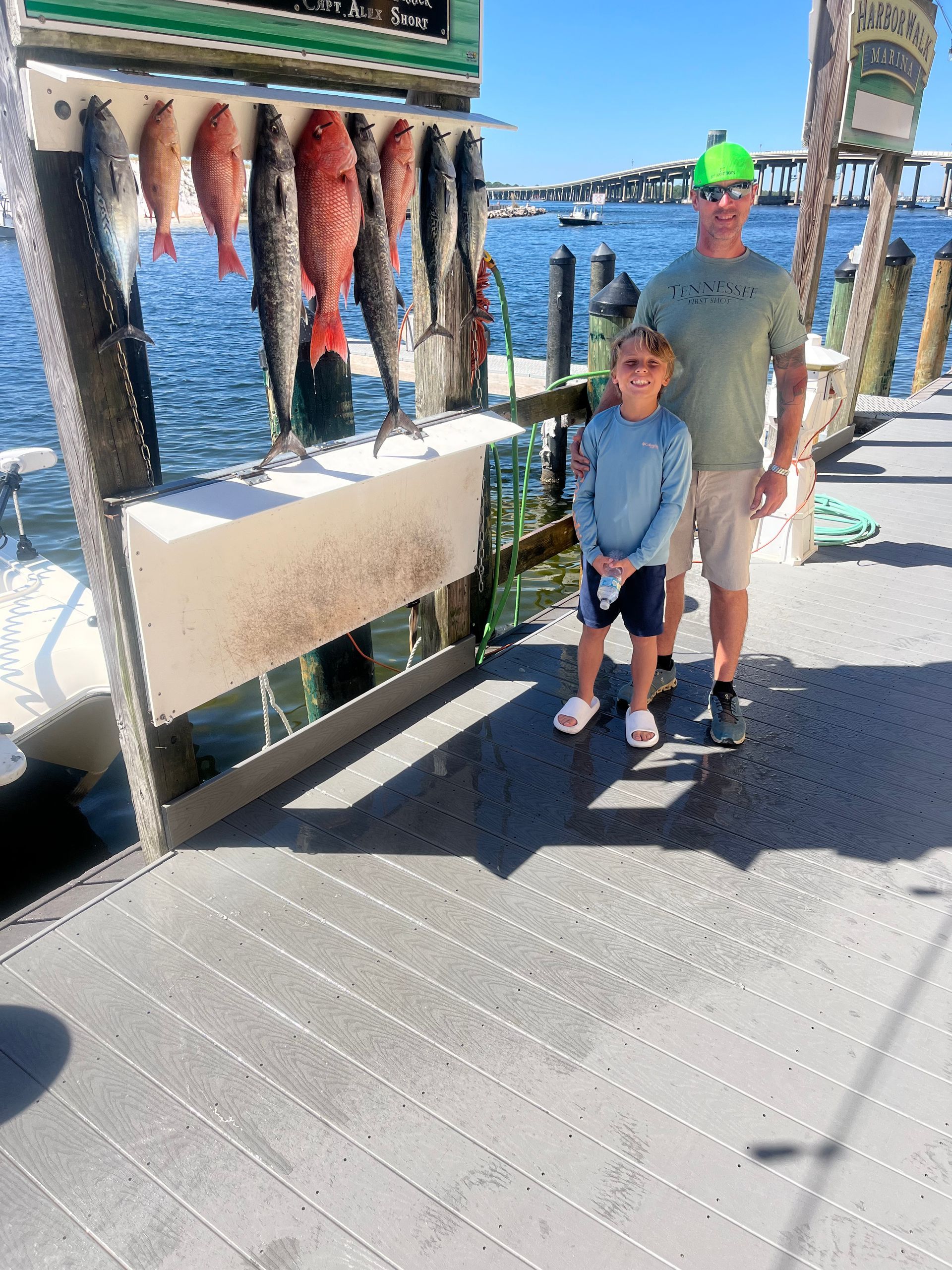 A man and a child are standing on a dock next to a display of fish.