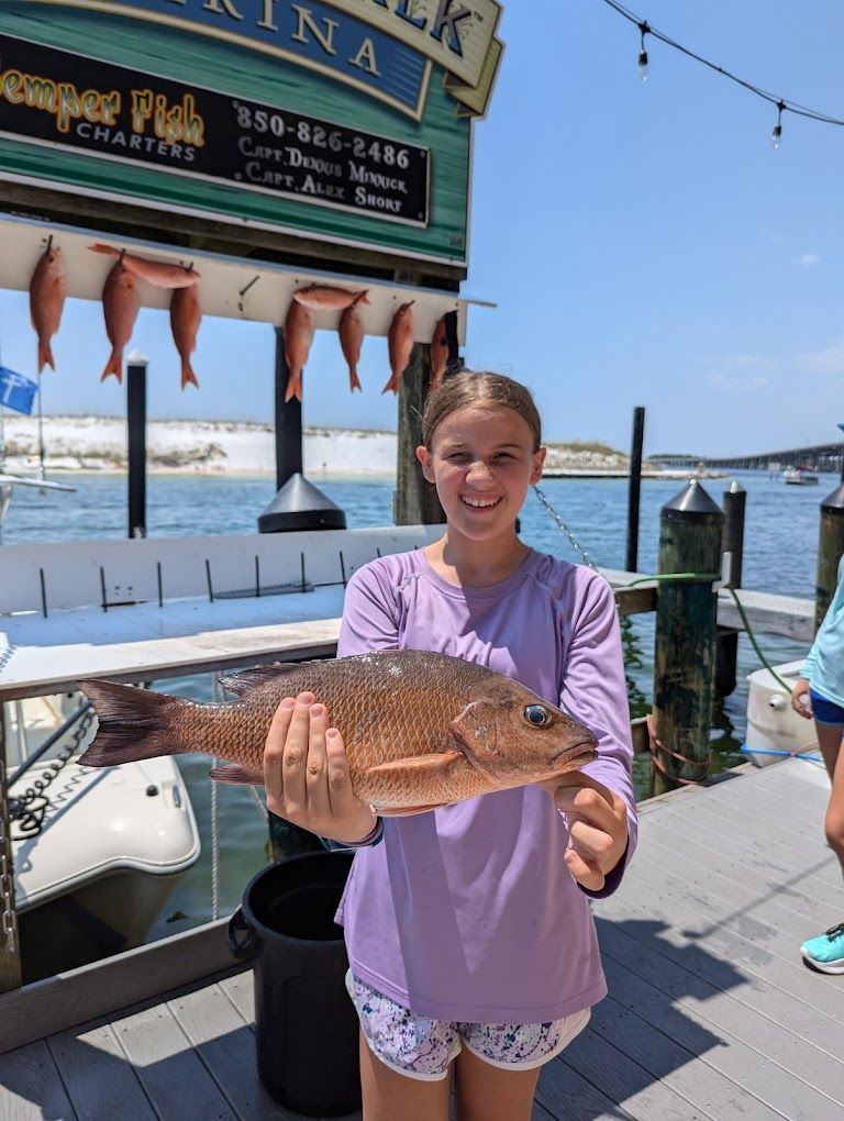 A young girl is holding a large fish on a dock.