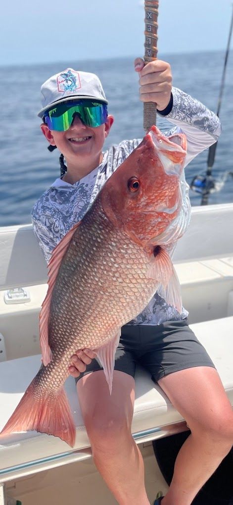 A young boy is holding a large red fish on a boat.