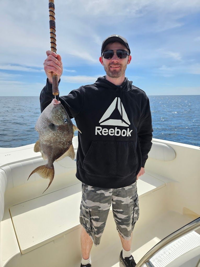 A man wearing a reebok sweatshirt is holding a fish on a boat.