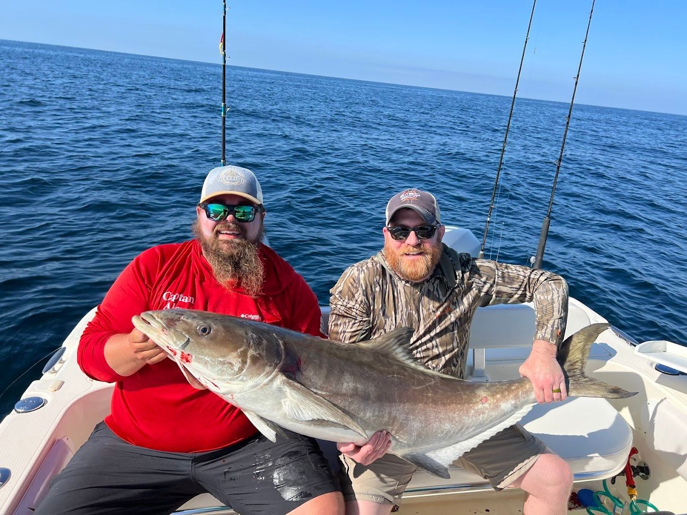 Two men are sitting on a boat holding a large fish.