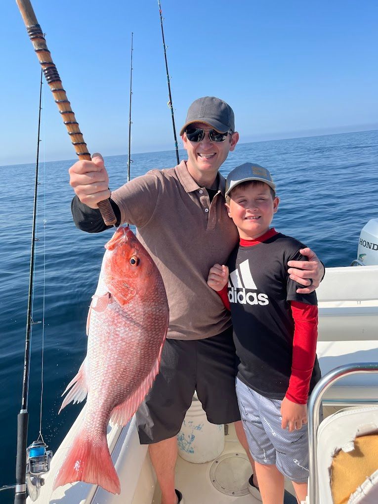 A man and a boy are standing on a boat holding a large fish.