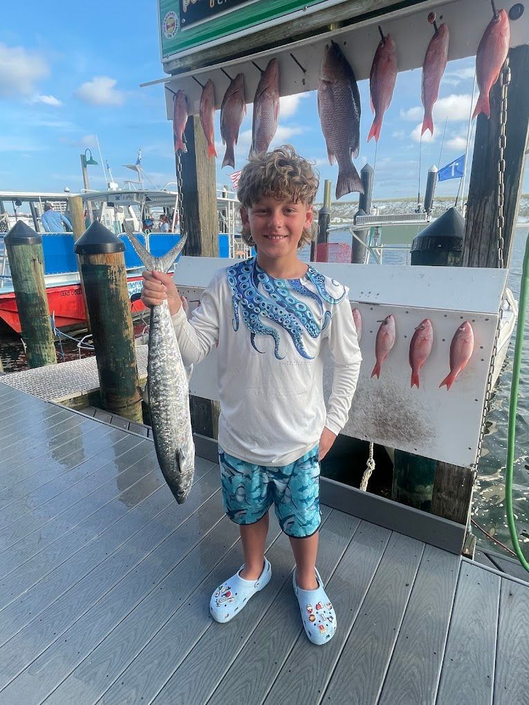 A young boy is holding a large fish on a dock.