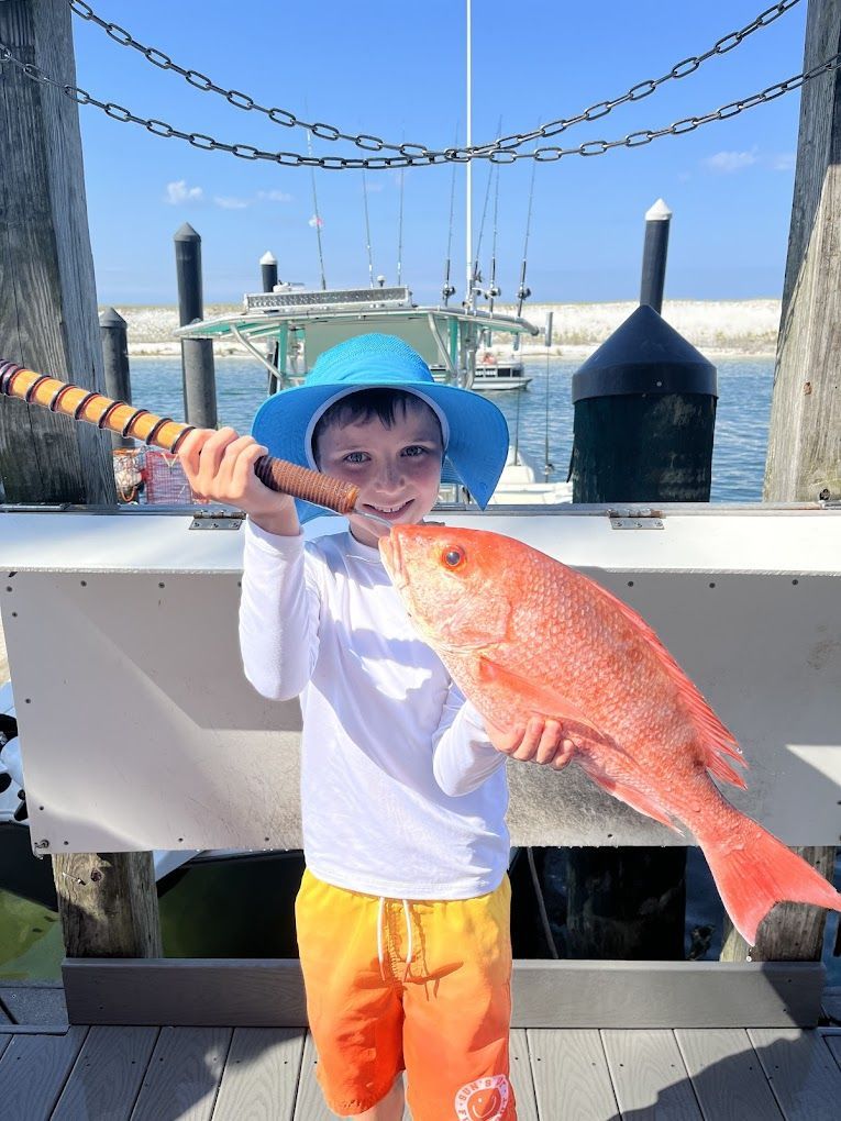 A young boy is holding a large red fish on a dock.