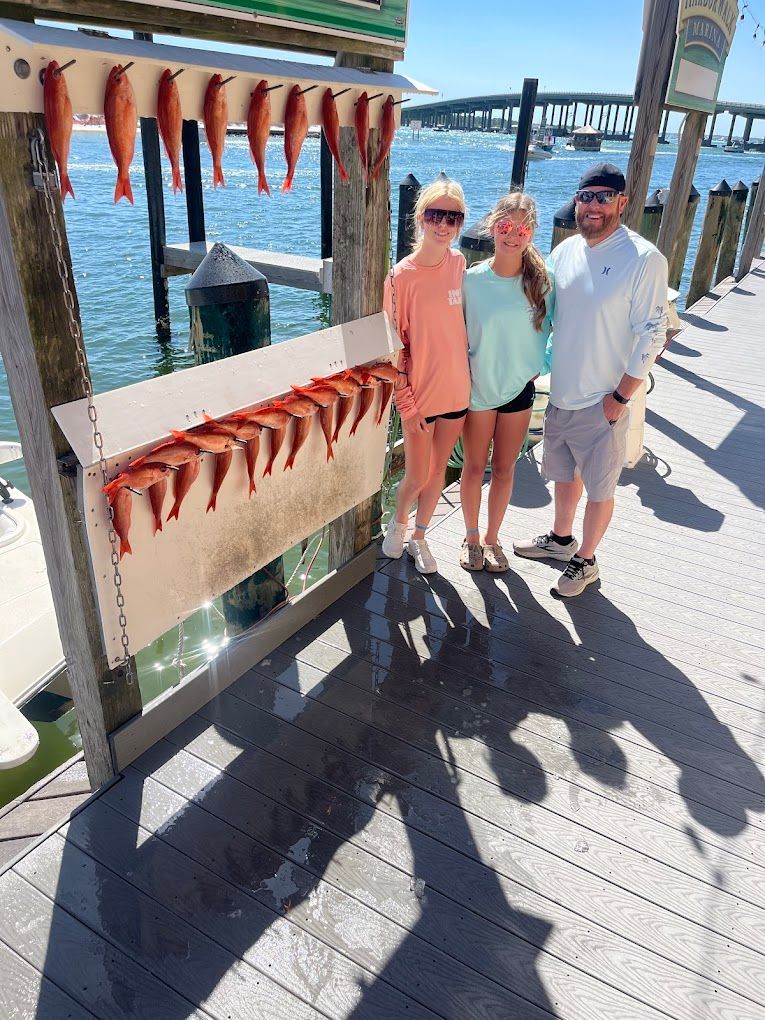 A group of people are standing on a dock with fish hanging from a rack.