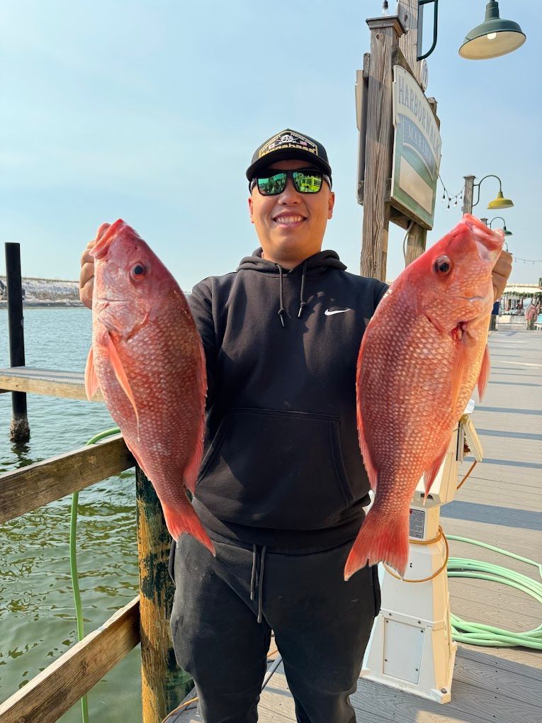 A man is holding two red fish on a dock.