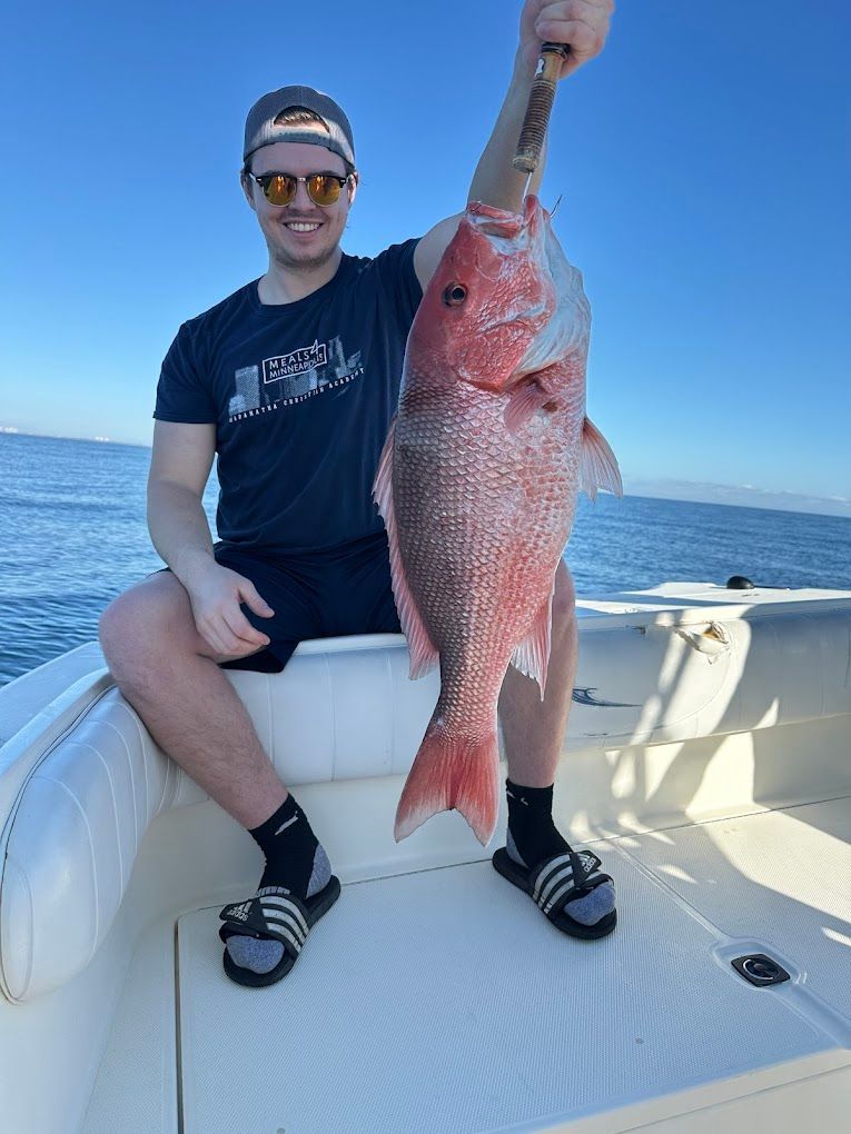 A man is sitting on a boat holding a large red fish.