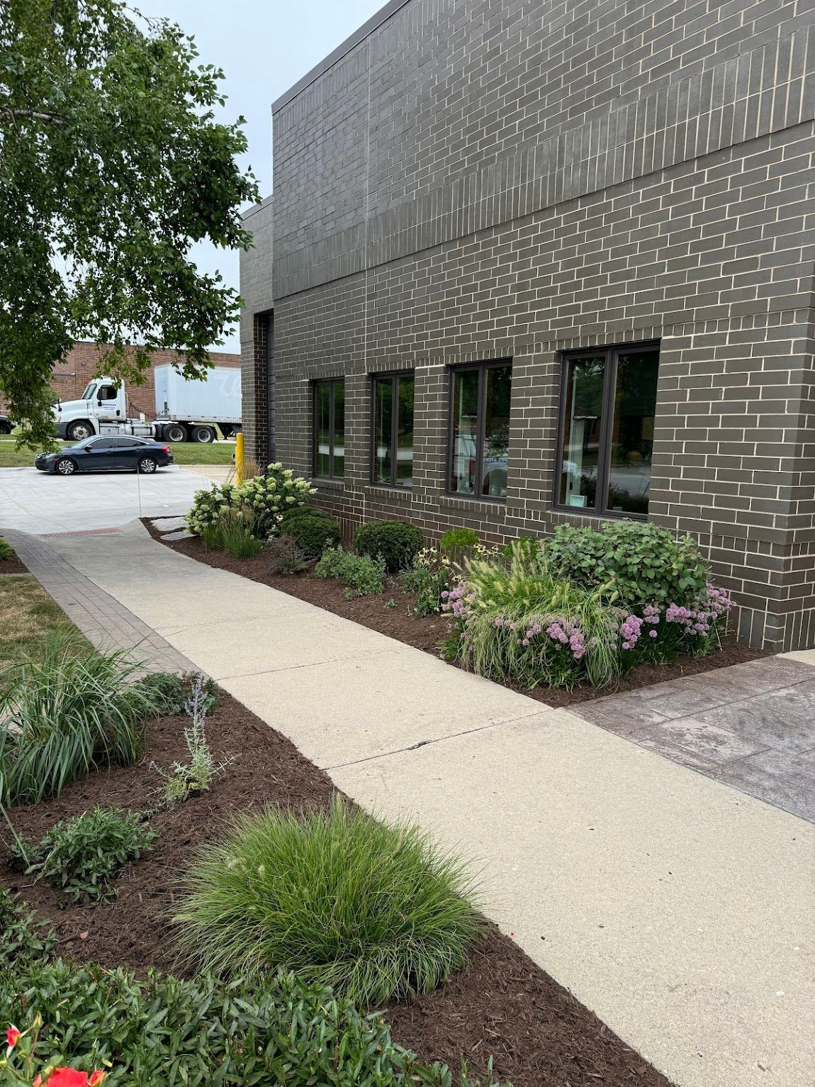 A brick building with a sidewalk and flowers in front of it.