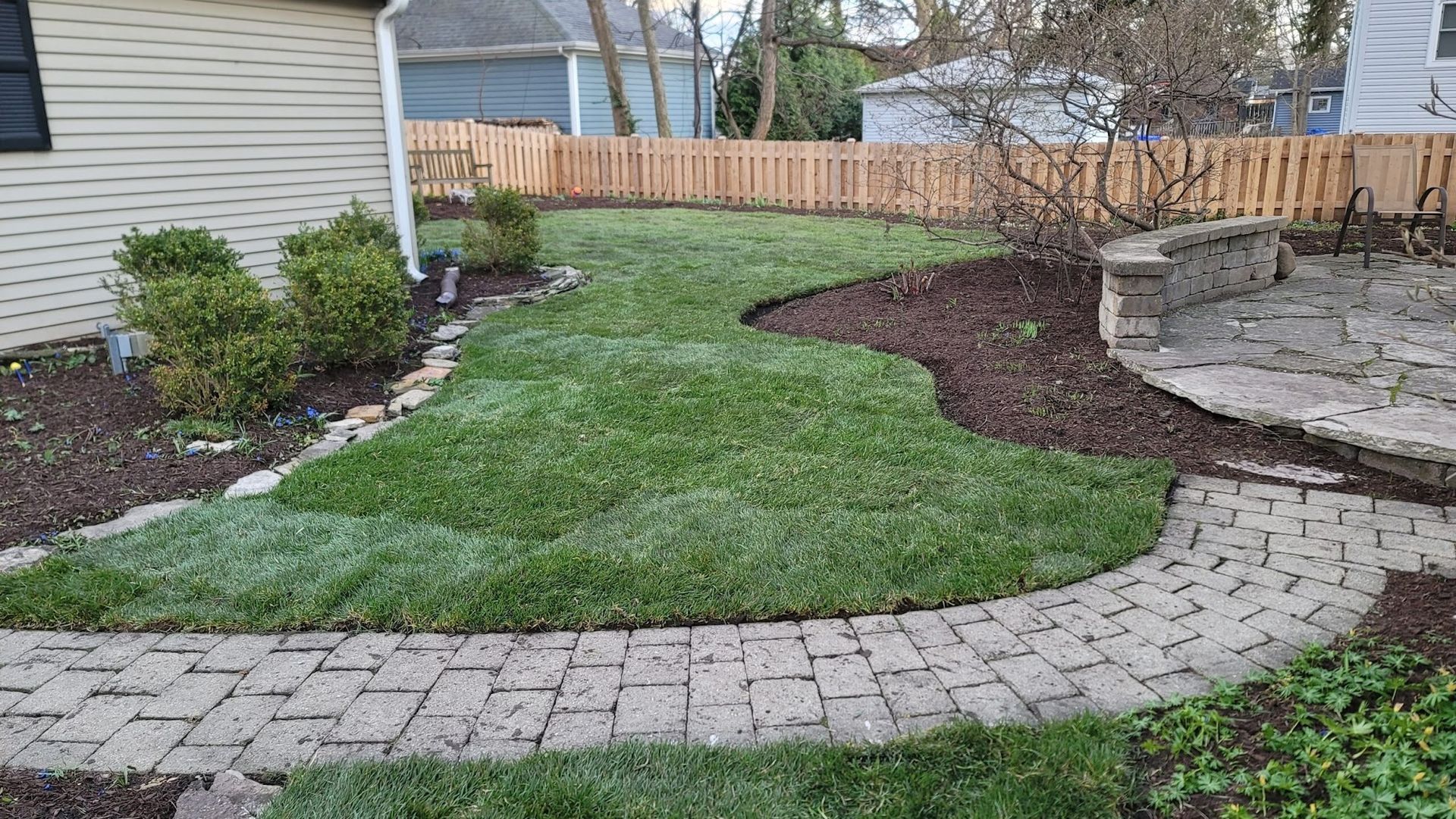 A backyard with a brick walkway and a wooden fence.
