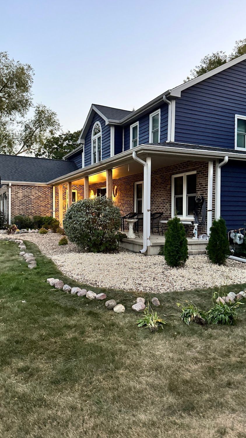 A large blue house with a porch and a lush green yard.
